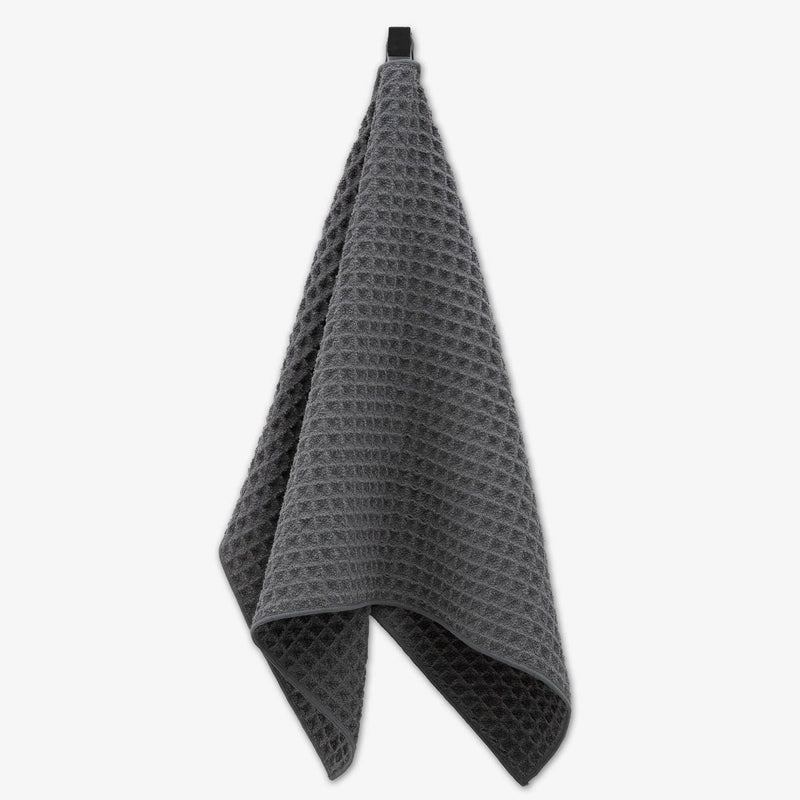 A dark gray waffle texture hand towel hanging from an attached fabric loop.