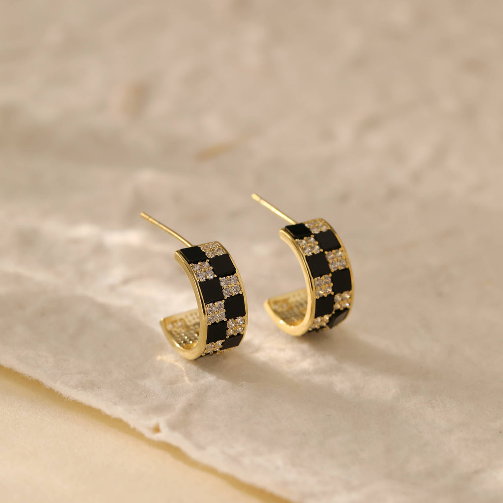 Two gold plated hoop earrings inlaid with white and black gems in a checkerboard pattern.