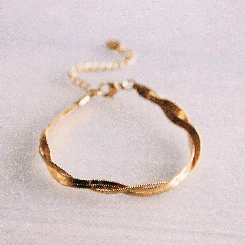 Two gold snake chains twisting around each other to make a single bracelet.