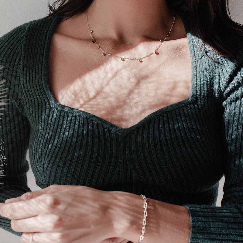 A person wearing the Rainbow Crystal Stardust Necklace in Gold with a hunter green knit top.