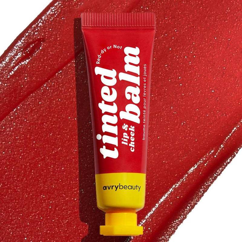 A red tube of Red-dy or Not Lip & Cheek Tint with a yellow cap in front of a swtch of red tinted balm.