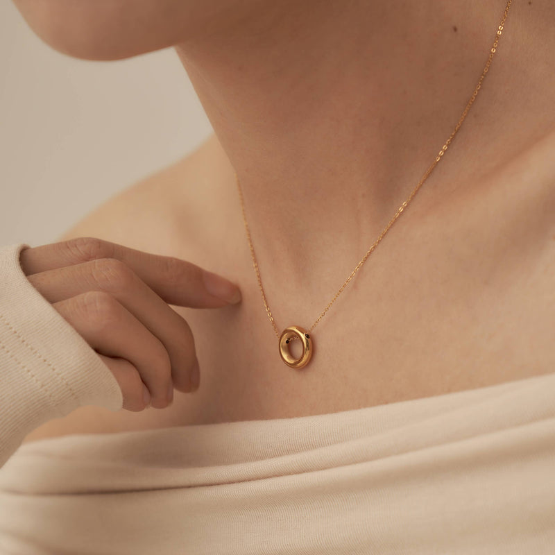 A person wearing a fine chain necklace with a gold plated stainless steel hollow hoop pendant.