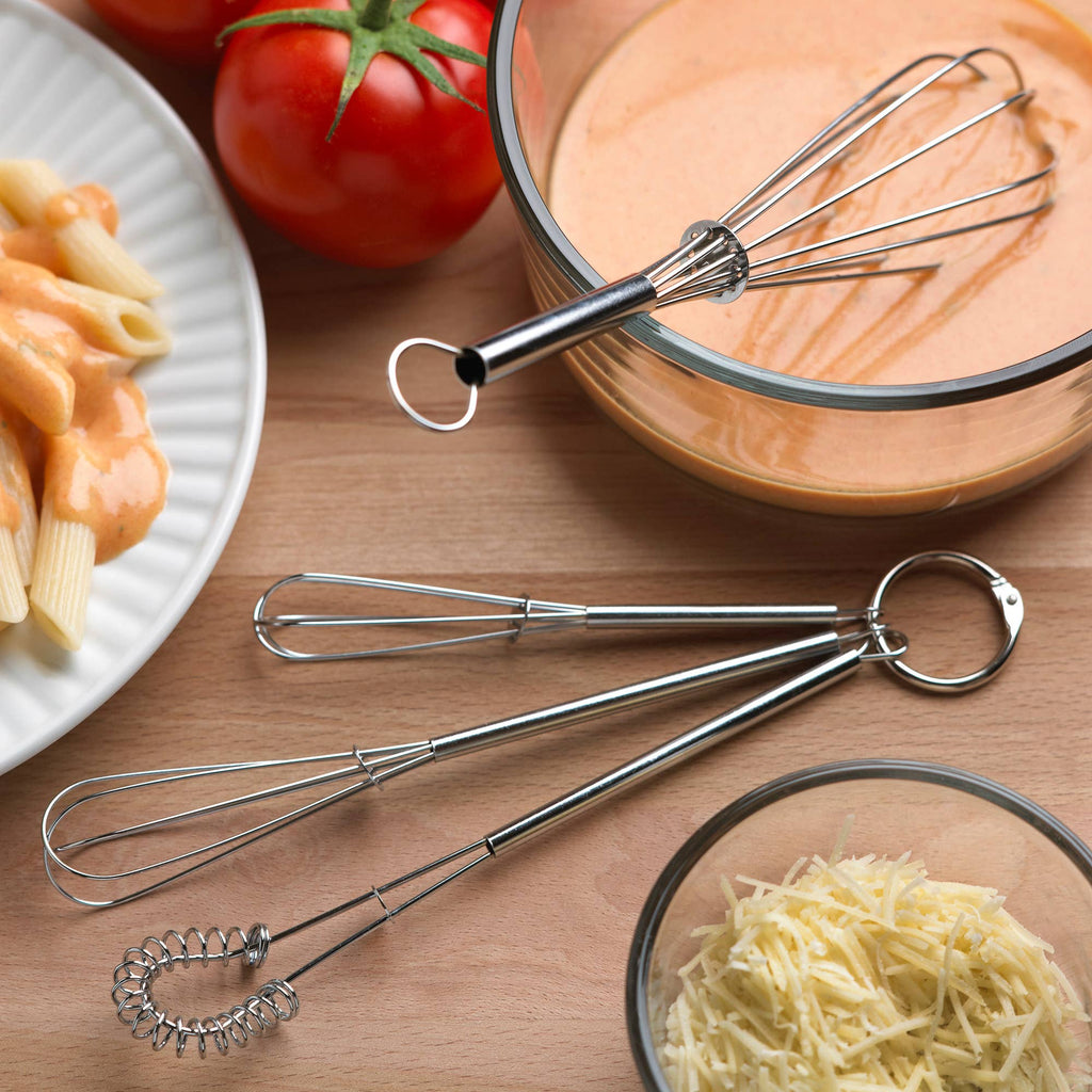 The largest whisk being used tomix pasta sauce while the other three whisks are on the table.