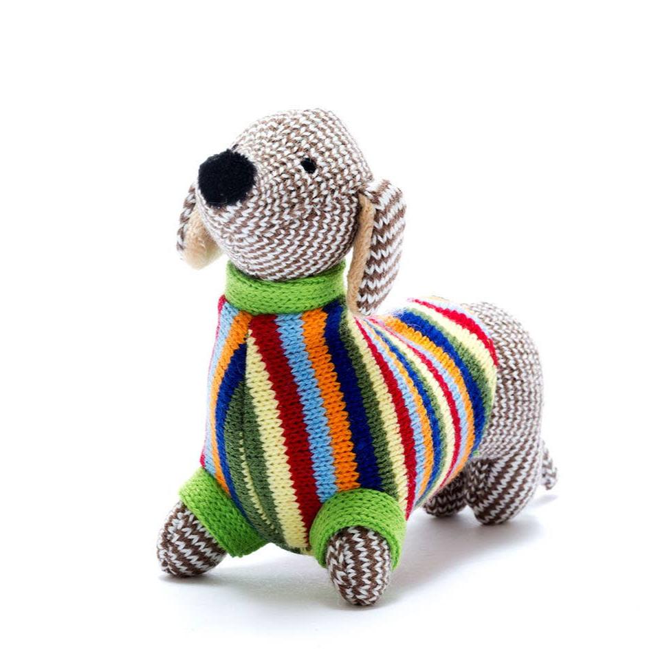 A brown and white knitted dachshund wearing a yellow, red, blue, orange, and green striped jumper.