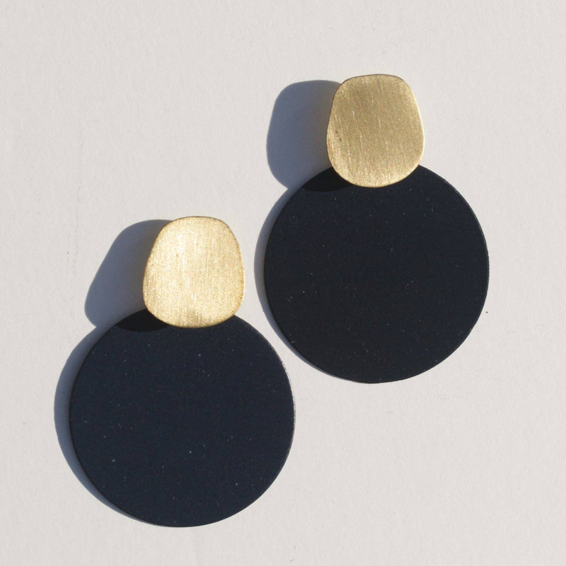 A pair of stud brass earrings with an oblong piece of brass and an ultramarine blue circle hanging from it.