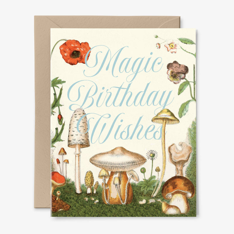 A cream birthday card illustrated with vintage mushrooms and flowers with "Magic Birthday Wishes" in pale blue script and a kraft envelope behind.