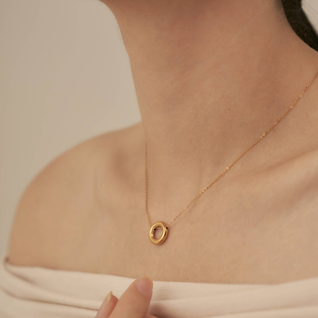 A person wearing a fine chain necklace with a gold plated stainless steel hollow hoop pendant.