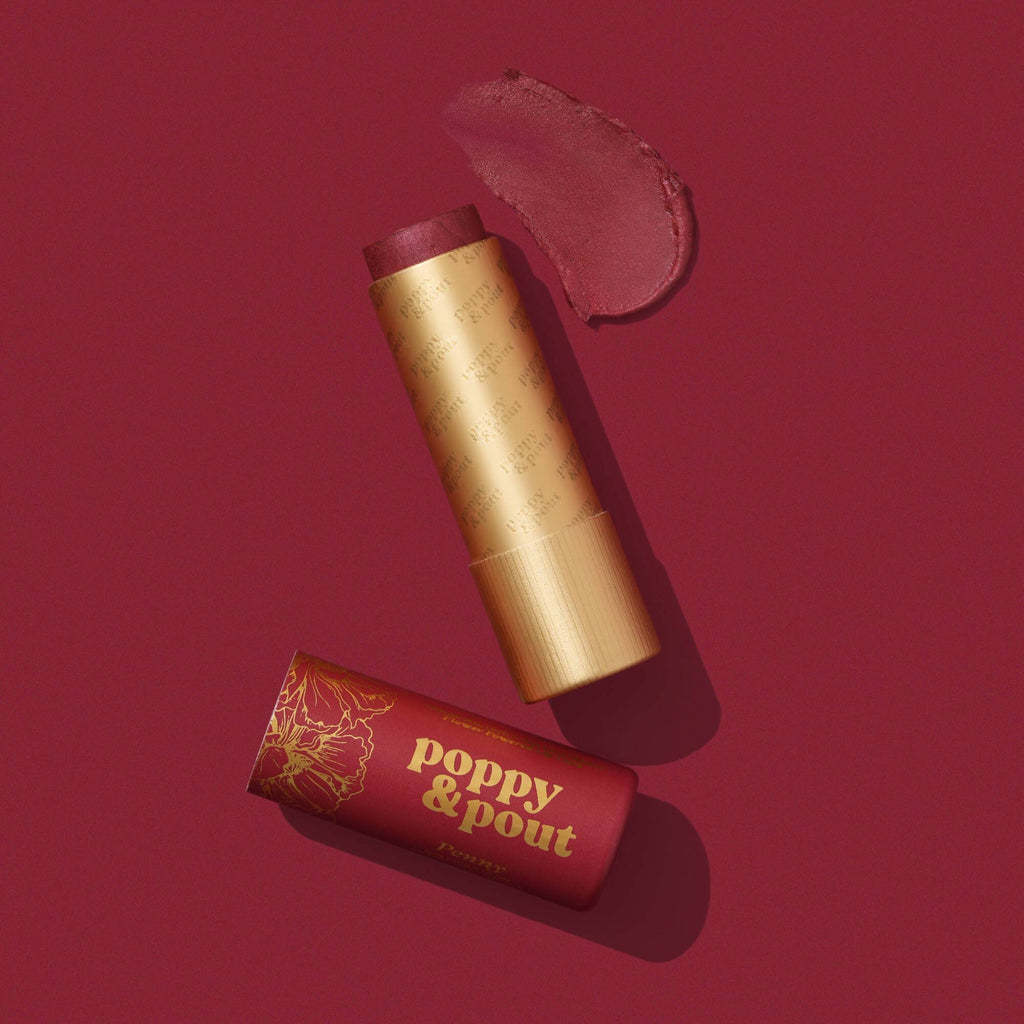 An opened deep red Penny Lip TInt next to its cap and a swatch against a similar red background.