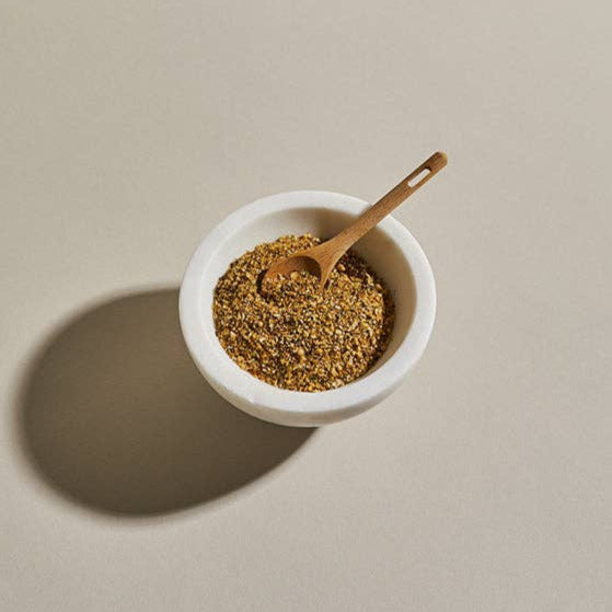 A white bowl filled with Salmon Seasoning with a wooden spoon dipping in.