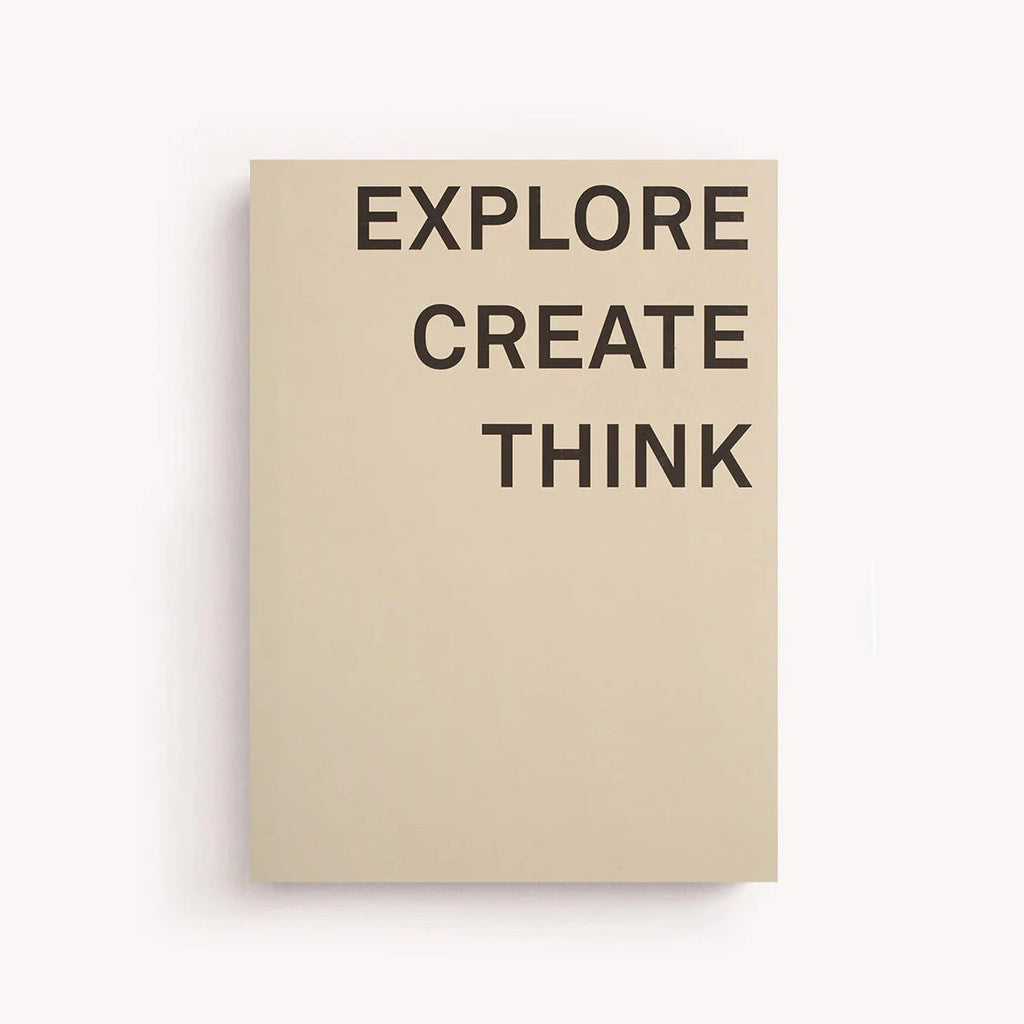 A large sand-colored notebook with the words "Explore. Create. Think." printed across the cover in black.