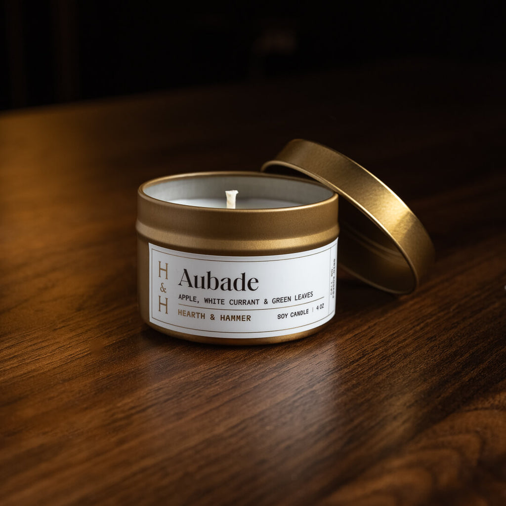 An open Aubade candle in an antique gold tin with its lid hanging off its side.