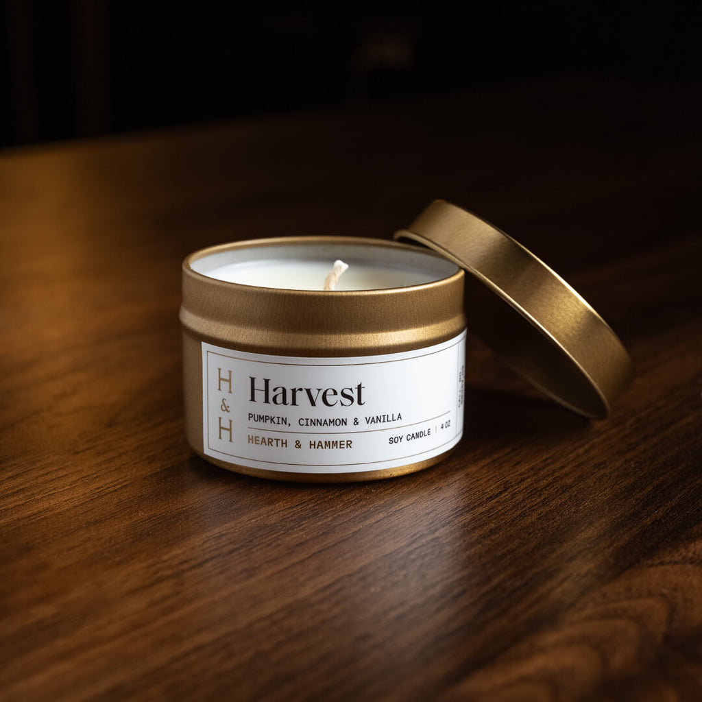 An open Harvest candle in an antique gold travel tin with its lid leaning against it.