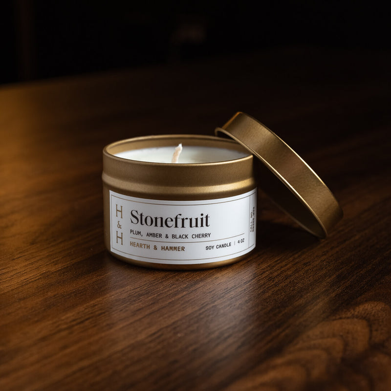 An open Stonefruit candle in an antique gold travel tin with it's lid hanging off the side.