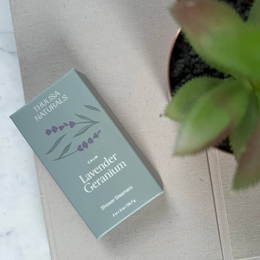 A box of lavender geranium shower steamers next to a fake potted plant.