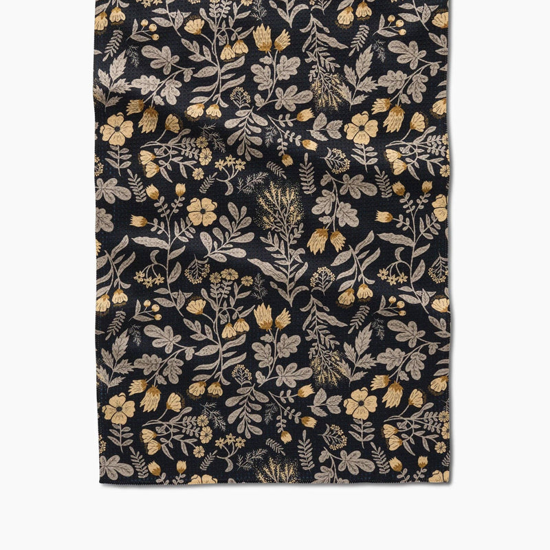 A black tea towelpatterned with yellow flowers with beige botanical details.