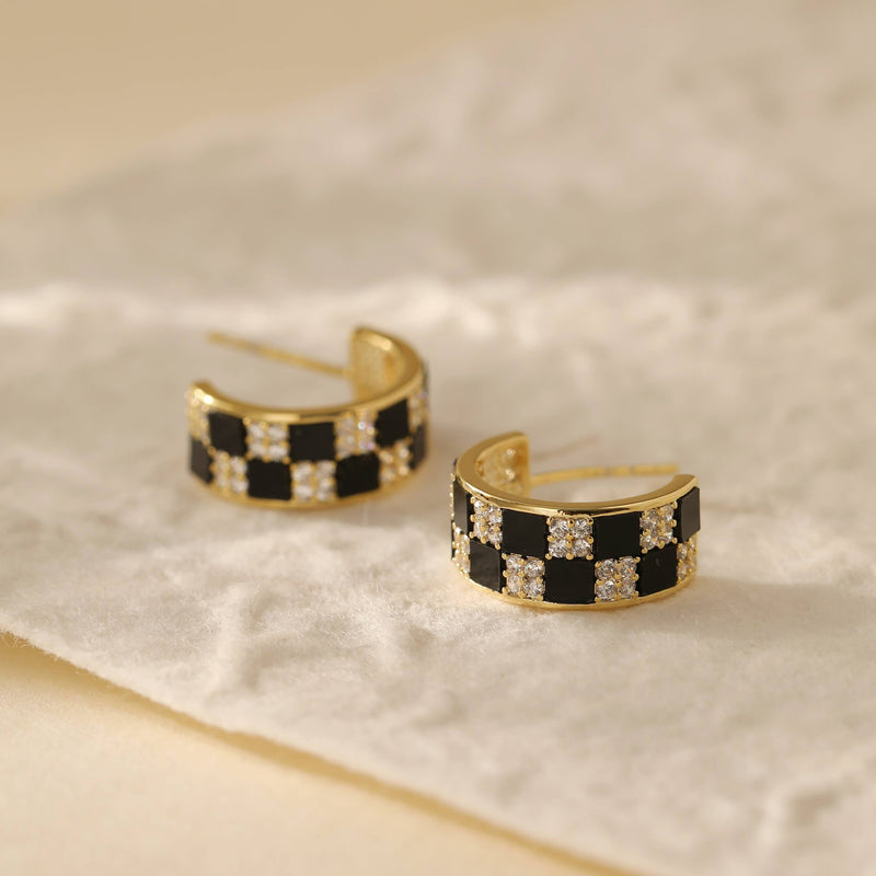 Two gold plated hoop earrings inlaid with white and black gems in a checkerboard pattern.