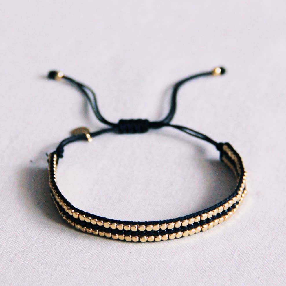 A black and gold beaded bracelet with black cord and a sliding knot closure.