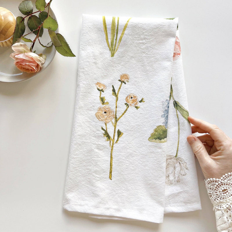 A hand holding the Garden Flowers Towel next to a dish washing brush and a pin rose on a white plate.