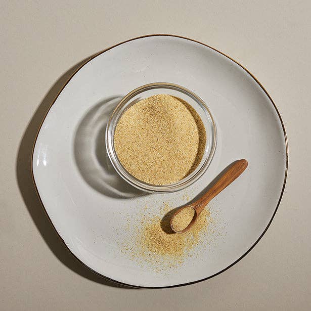 A glass bowl of Granulated Garlic with a wooden spoon spooning it out on a plate.