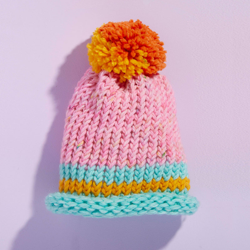 A pink, orange, and teal knitted hat with a pom pom.