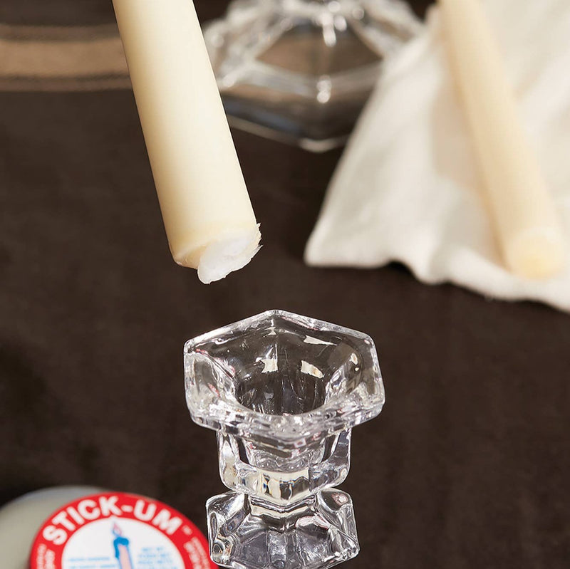 A candle taper with a bit of candle adhesive at the bottom being attached to a glass candleholder.