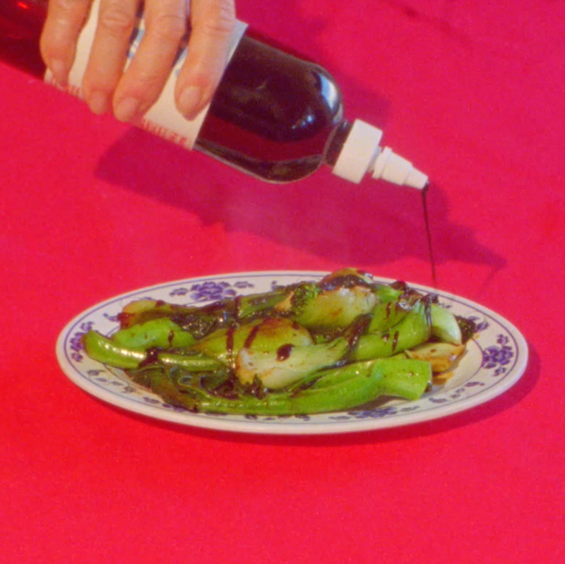 A hand squeezing some Woon Stir Fry Sauce onto a plate of veggies.