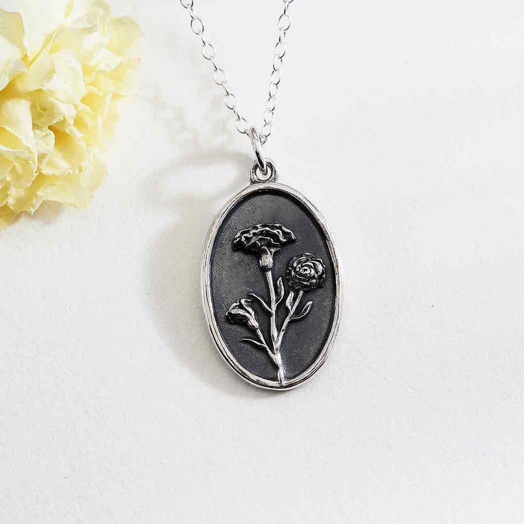 A silver necklace with a carnation flower on an oval pendant.