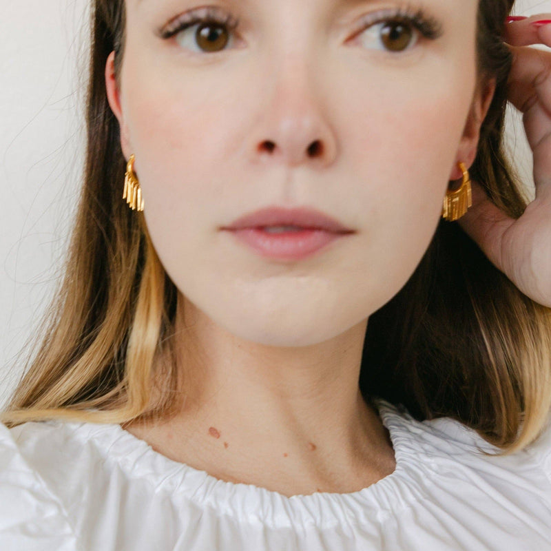 A person wearing the Fringe with Benefits Hoops in Gold.