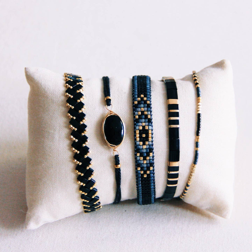 A pillow wrapped with black and gold bracelets, including the Obsidian Twisted Bracelet.