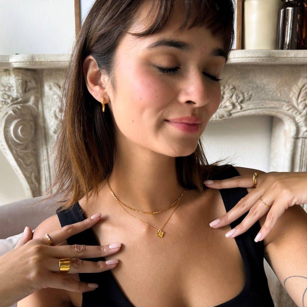 A person smiling with their eyes closed while wearing the Butterfly Necklace in Gold stacked with a fine chain.