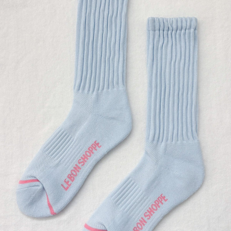 A pair of pale blue long crewneck socks with a pink stripe at the toe and "Le Bon Shoppe in pink below the foot.