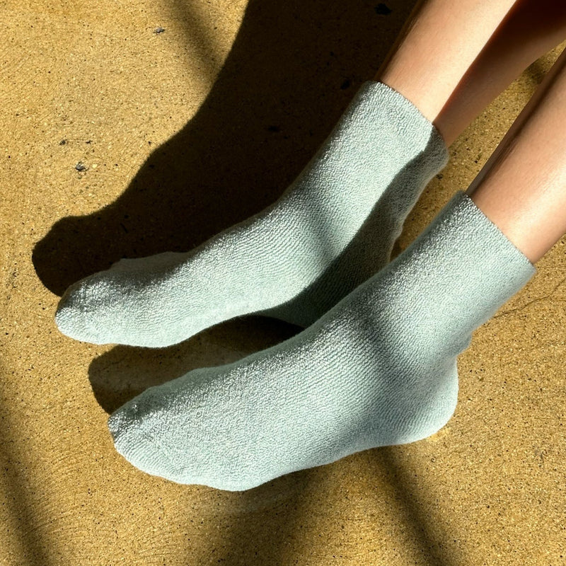 A person wearing light green fluffy socks on their feet.