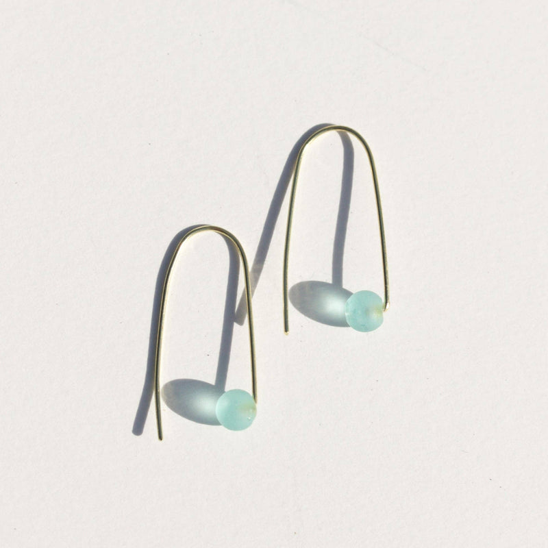 A gold plated brass threader pair of earrings with a ball of light blue sea glass at the end.