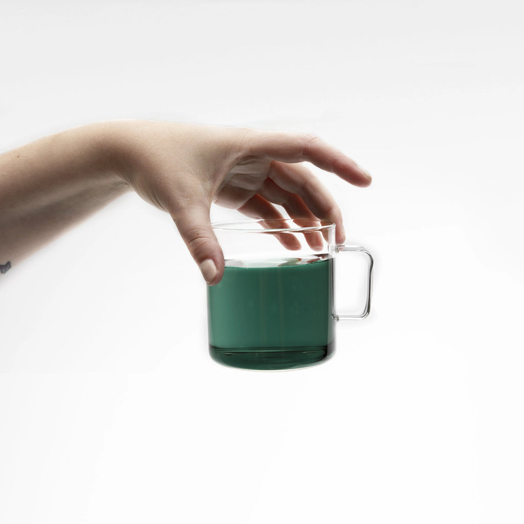 A hand holding a clear mug of blue tea.