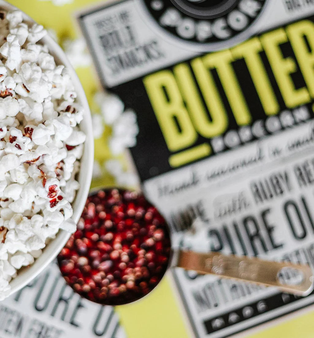 A bowl of butter popcorn next to a scoop of corn kernels.