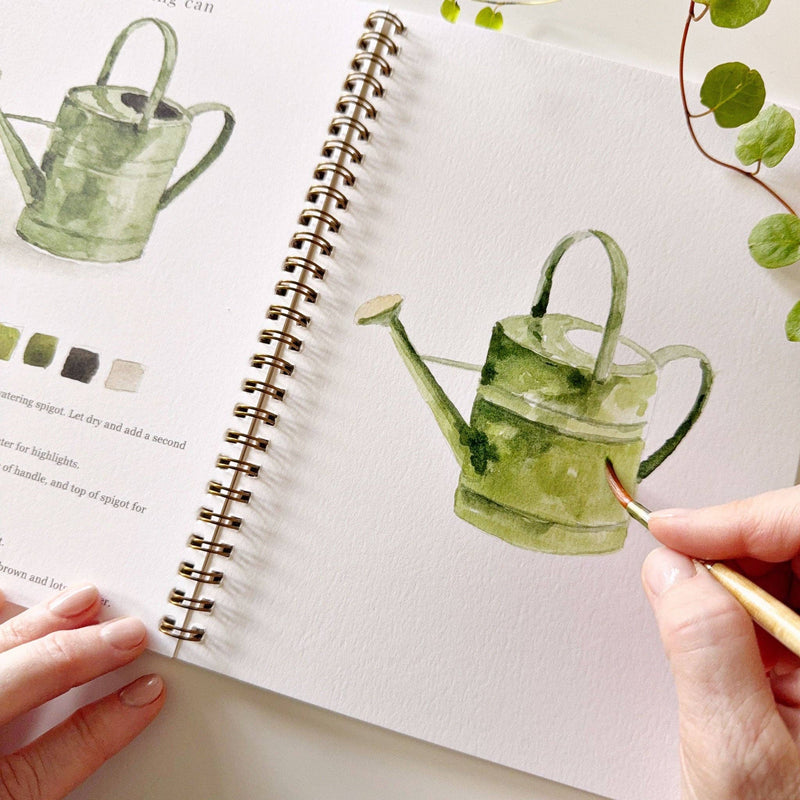 A pair of hands watercolor painting a green watering can.