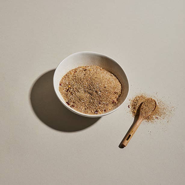 A ceramic bowl of Pilsen Spicy Adobo Blend seasoning with a wooden spoon.