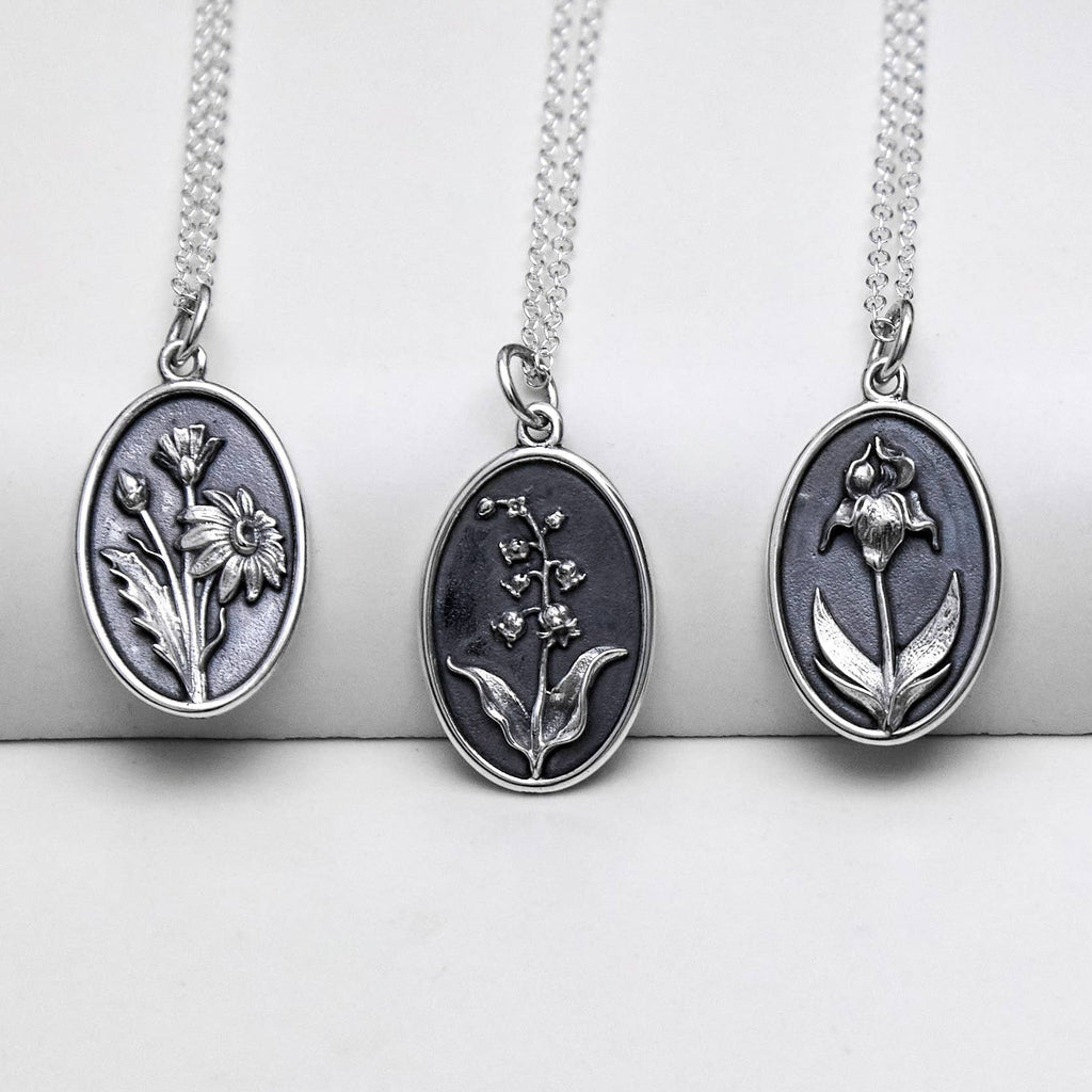 Three silver oval necklaces, each with a different birth month flower embedded into the center.