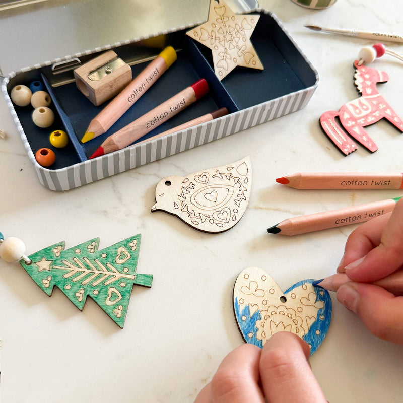 A pair of hands drawing on a wooden heart ornament with a color pencil.