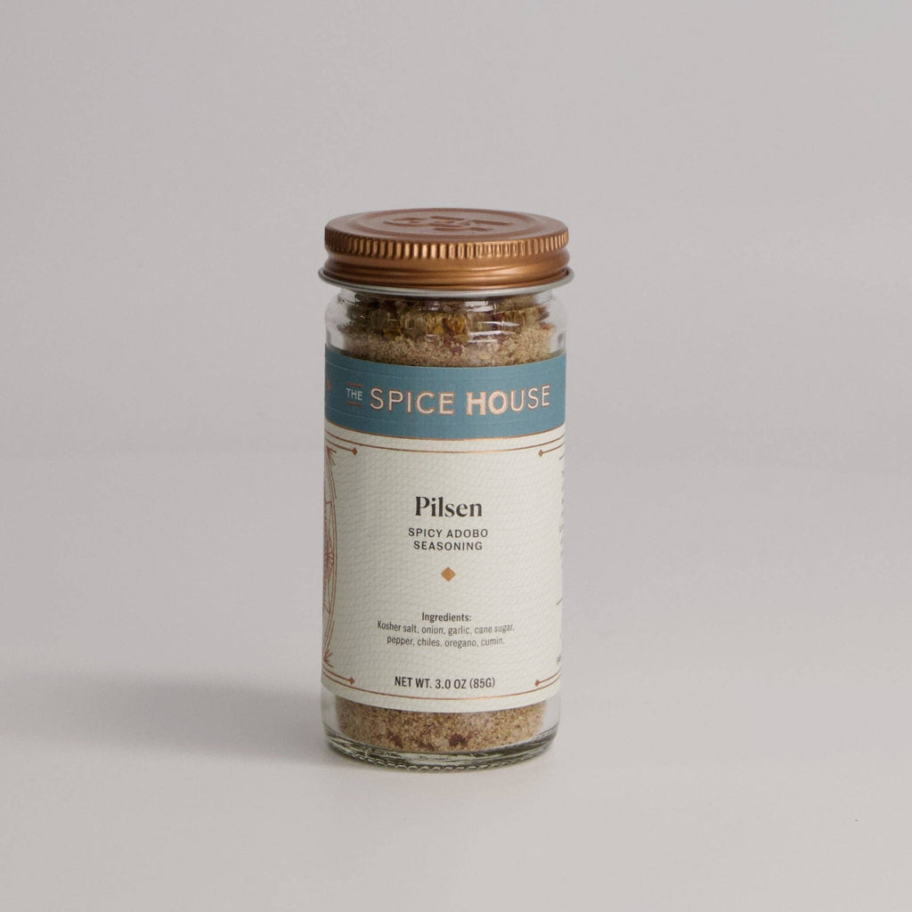 A glass jar of Pilsen Spicy Adobo Seasoning covered with a copper lid.