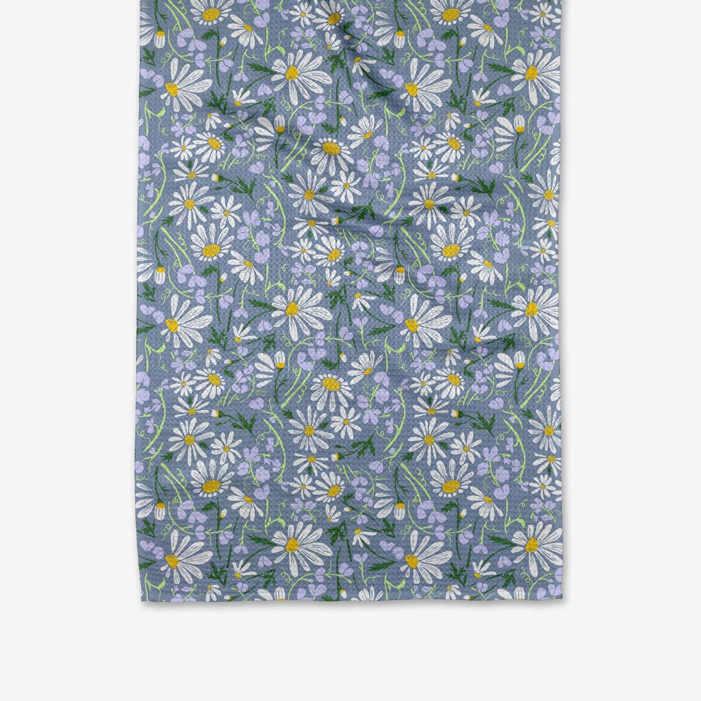 A gray blue tea towel patterned with purple flowers, white daisies, and other green botanicals.