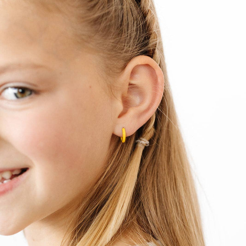 A young girl wearing the Enamel Hoops in Yellow.