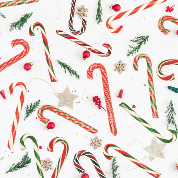 A clutter of candy canes surrounded by sprigs of cedar, glitter stars, red ornaments, and wooden snowflakes.