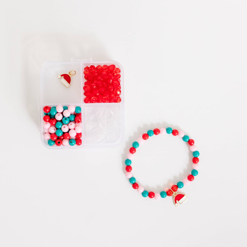 A storage box filled with red, green, and pink beads, a Santa hat charm, and stretch cord next to a finished bracelet.