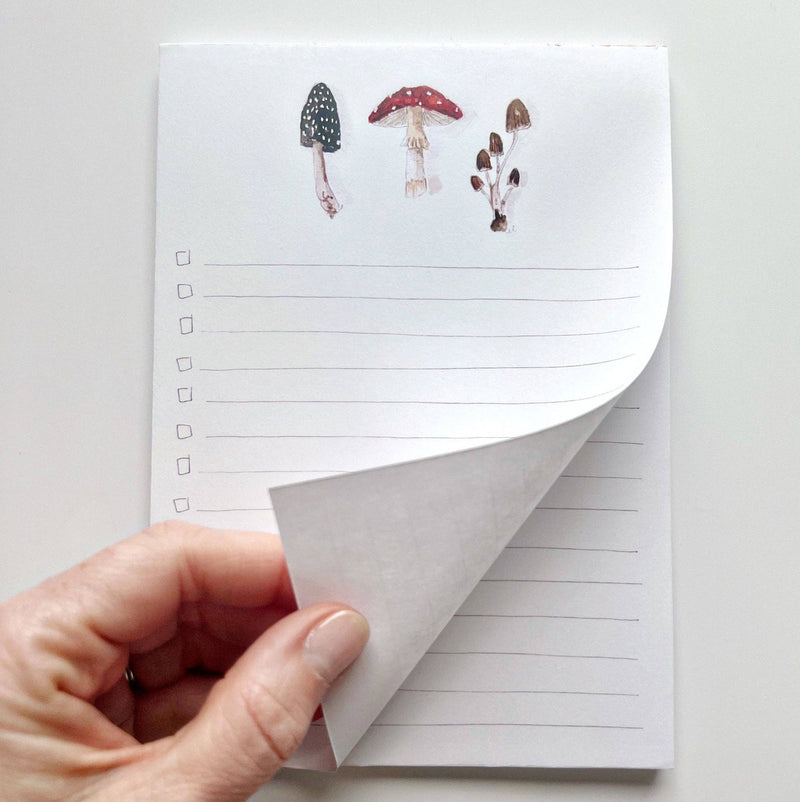 A hand lifting up a page of the Mushroom Checklist Notepad.