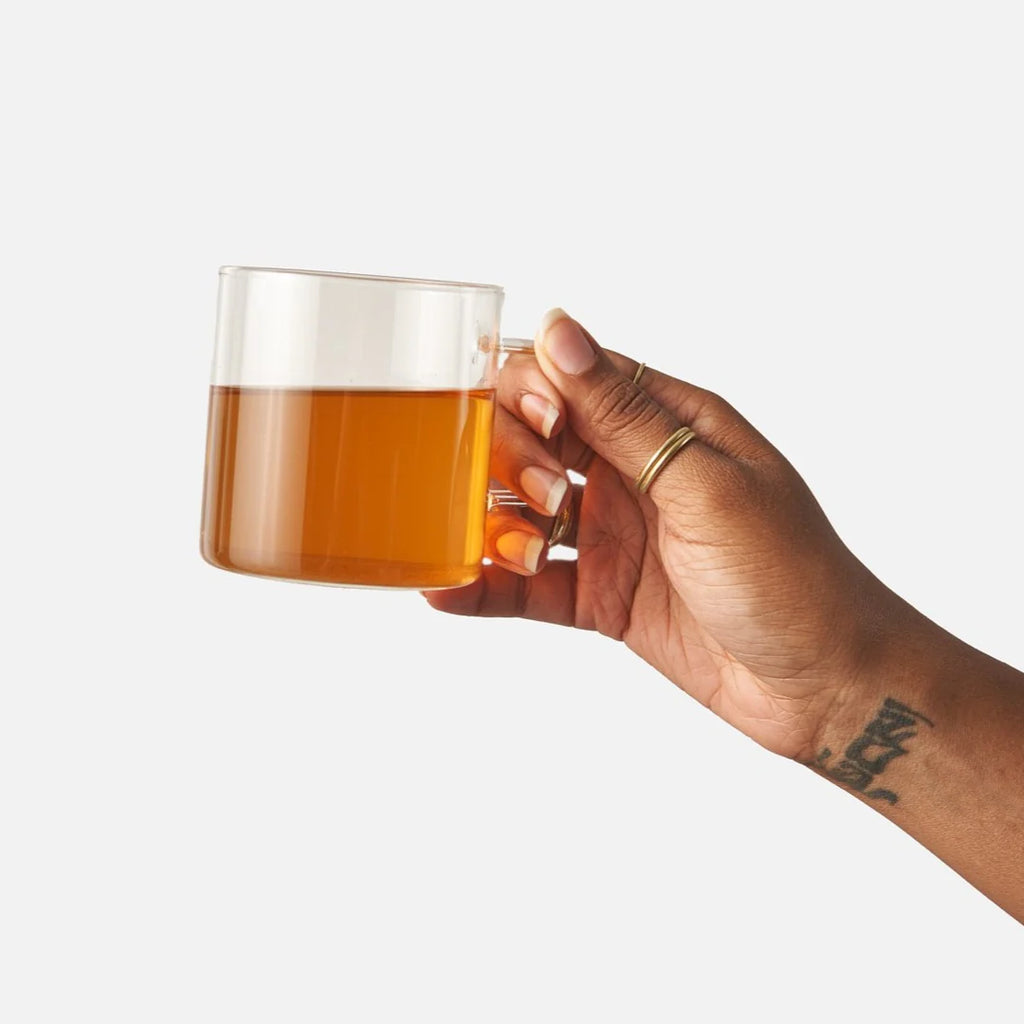 A hand holding a glass mug filled with freshly brewed Cozy Night tea.