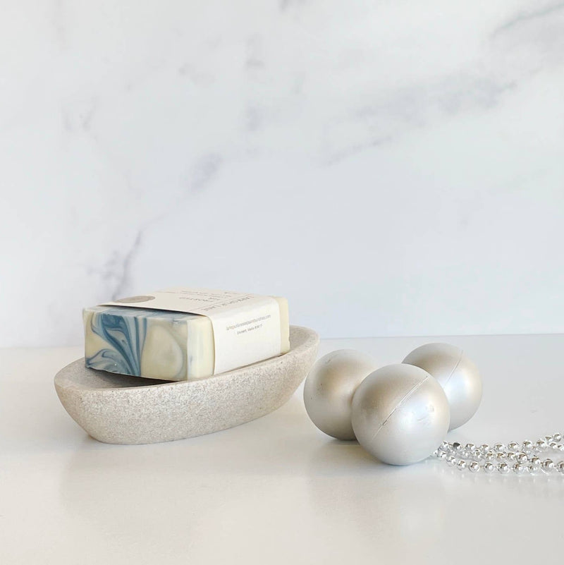 A bar of Frosted Fir Soap on a stoneware soap holder next to a trio of silver ornaments.