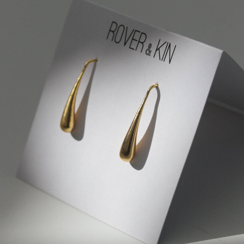 The gold drop earrings resting in its folded paper packaging.