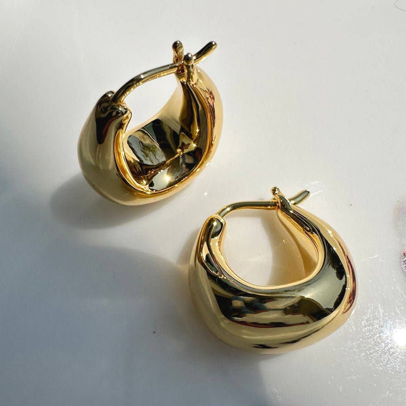 A pair of gold plated hoops with the bottom of the hoop being a thick slightly uneven dumpling shape.