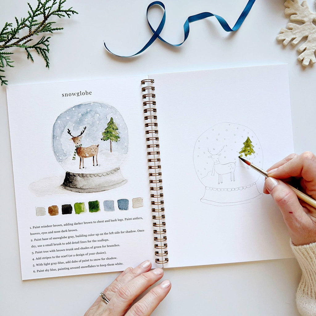 A person watercolor painting an evergreen tree in the watercolor workbook.